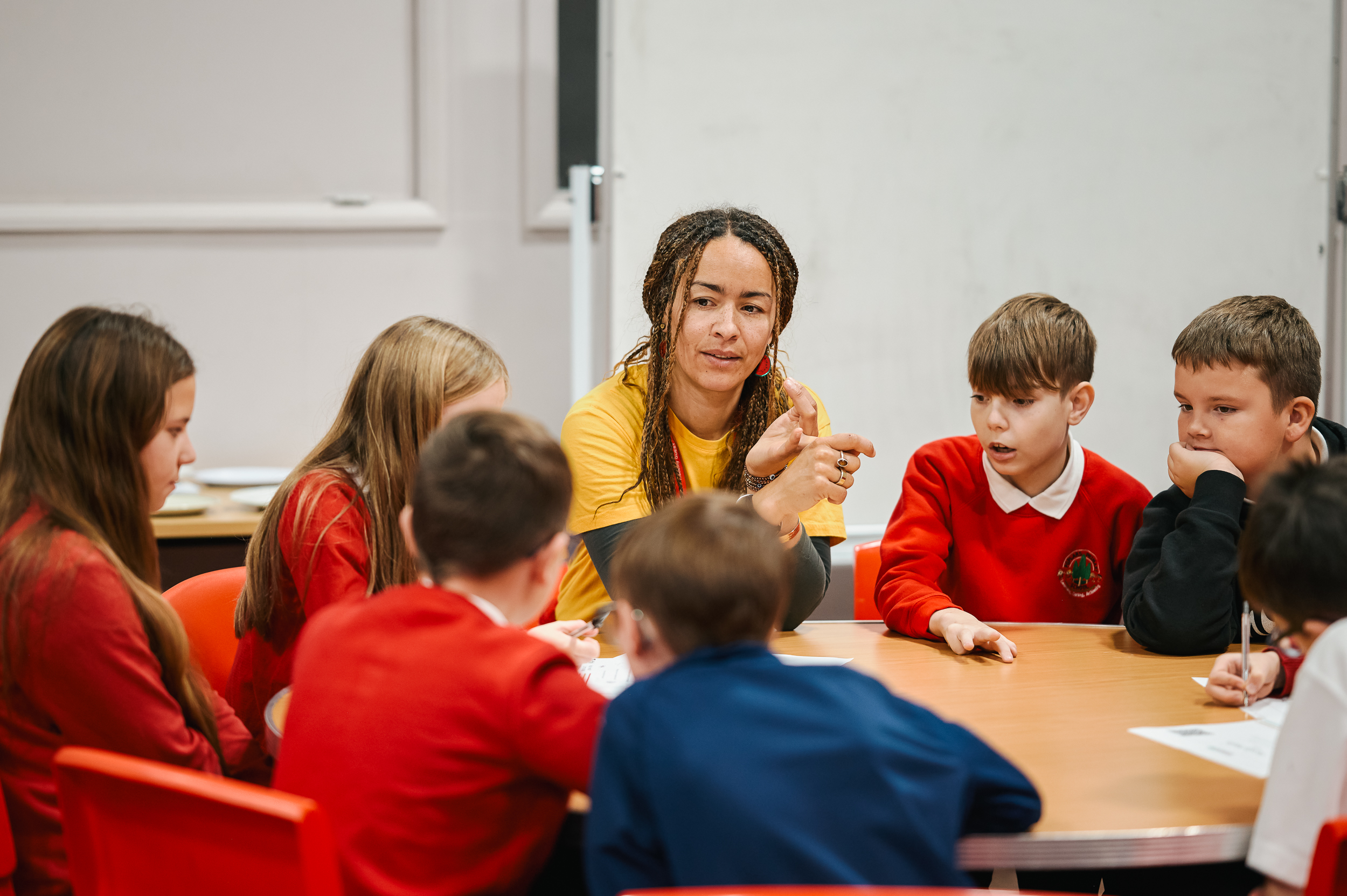 School children discussing something with a leader sat at school tables