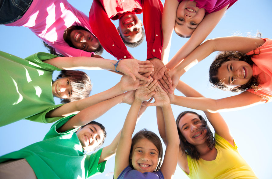 A group of eight children looking down into camera with hands meeting in middle to form a star shape.