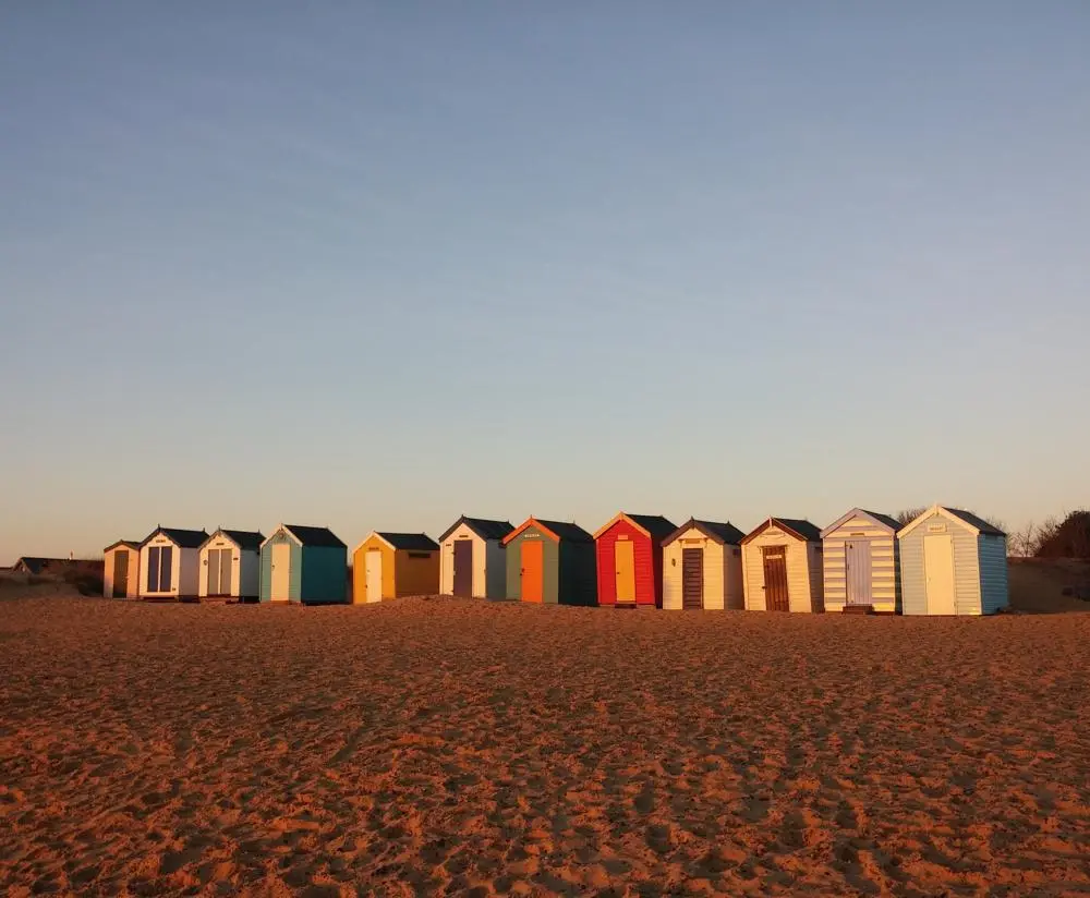 A selection of Suffolk beach huts on a sandy beach at sunset.