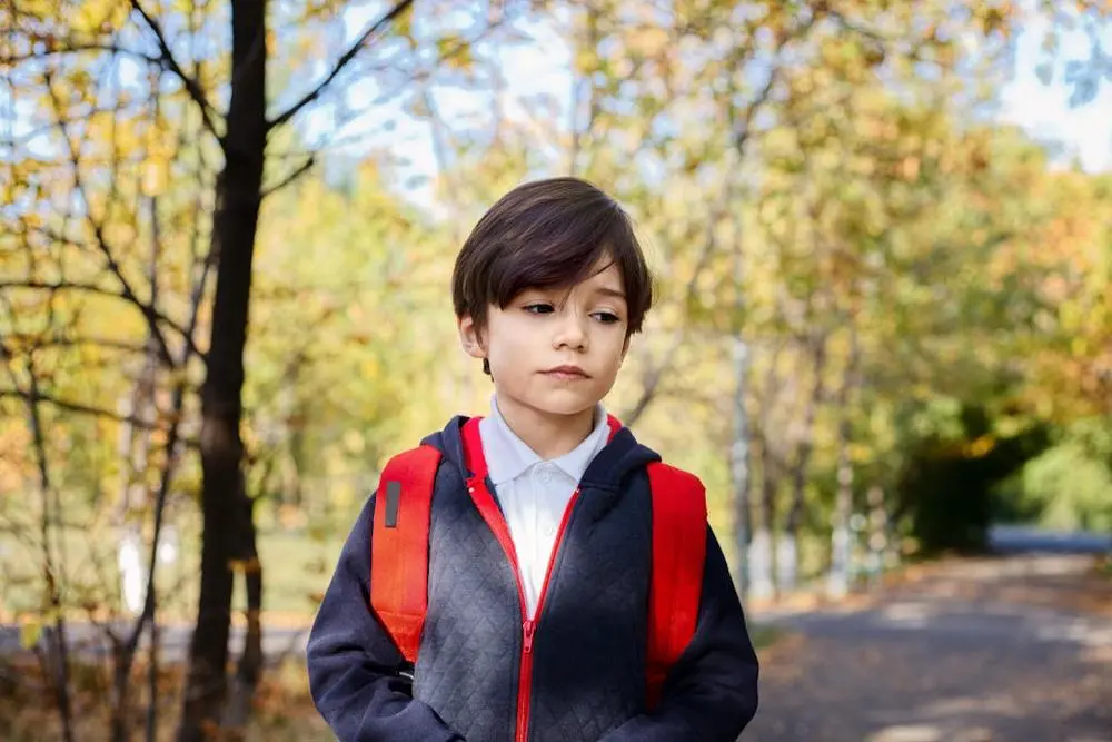 Young boy with rucksack walking through park.